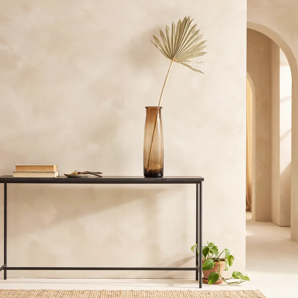 Single dried palm spear in smoked glass vase on console table
