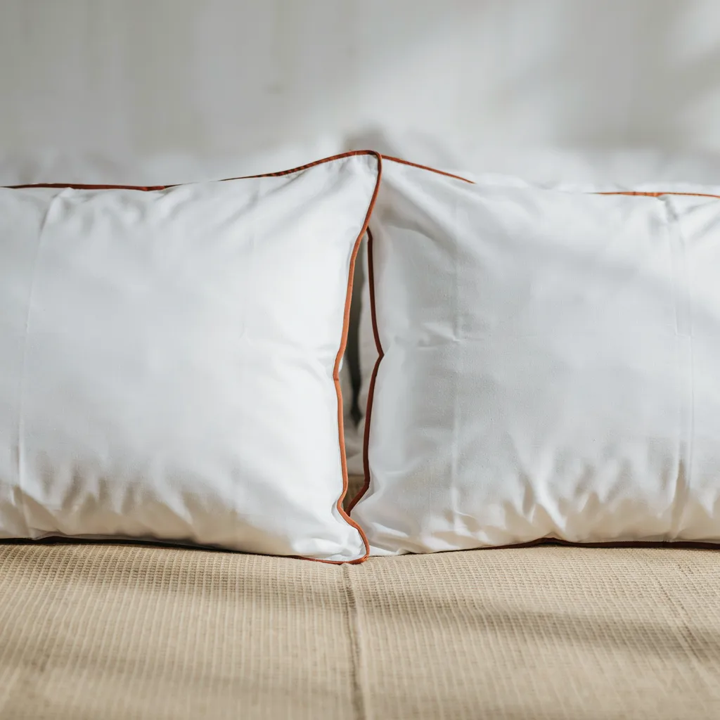 White percale pillowcases with thin terracotta contrast piping on twin XL dorm bed with warm oat waffle-weave duvet