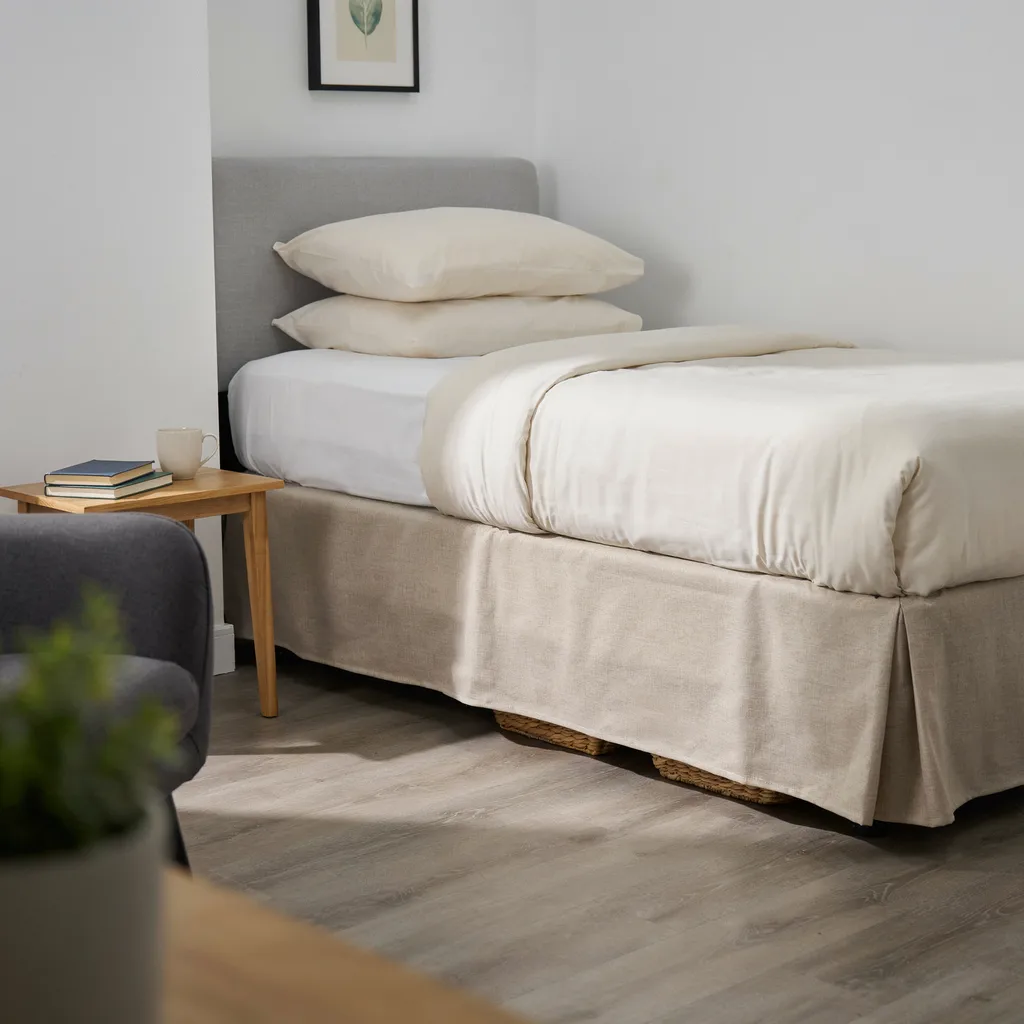 Extra-long flat-panel linen bed skirt dropping to floor concealing storage bins under twin XL dorm bed with cream duvet